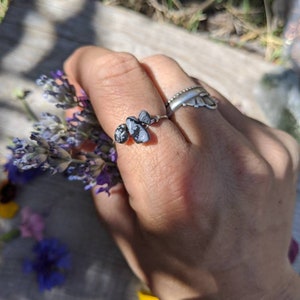 May include: A silver ring with a cluster of three black and white snowflake obsidian stones. The ring is worn on a person's finger.