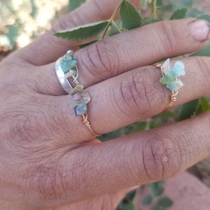 May include: Two rings with green and brown stones wrapped in gold wire. The rings are on a person's finger.