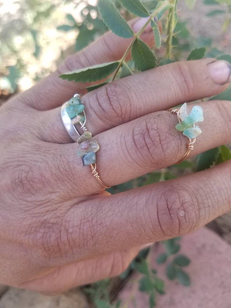 May include: Two rings with green and brown stones wrapped in gold wire. The rings are on a person's finger.