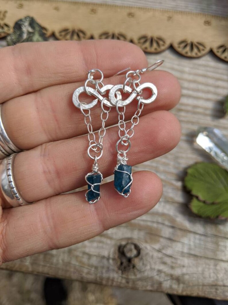 May include: Silver infinity symbol earrings with a dangling blue apatite crystal on each earring.