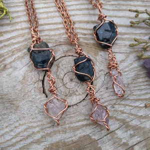 May include: Three copper wire wrapped necklaces with black and purple gemstones. The necklaces are hanging on a wooden surface.