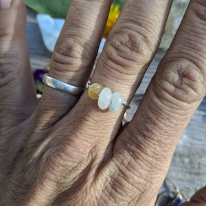 May include: A silver ring with three round beads. The beads are yellow, white, and light green.