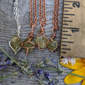 May include: Four necklaces with green gemstone pendants wrapped in copper wire. The necklaces are on a wooden surface with lavender flowers and a yellow flower.