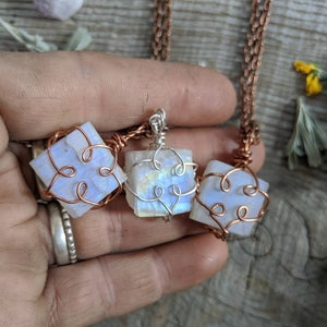 Puede incluir: Tres colgantes de piedra lunar iridiscente envueltos en alambre de cobre, cada uno con un dise&ntilde;o diferente. Los colgantes est&aacute;n enhebrados en una cadena de cobre.