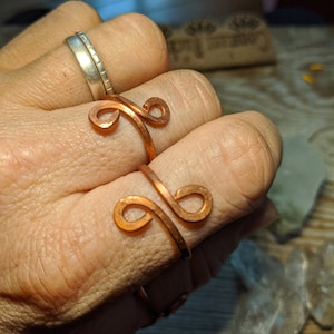 May include: Two copper wire rings with a unique design. The rings are worn on a finger.