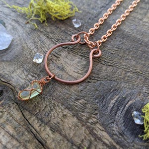 Könnte beinhalten: Ein Anhänger aus grünem Stein, der mit Kupferdraht umwickelt ist, hängt an einem Hufeisen-Anhänger aus Kupferdraht an einer Halskette aus Kupfer.
