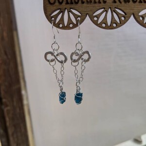 May include: A pair of silver infinity symbol earrings with a dangling chain and a dark blue gemstone at the end of each chain.
