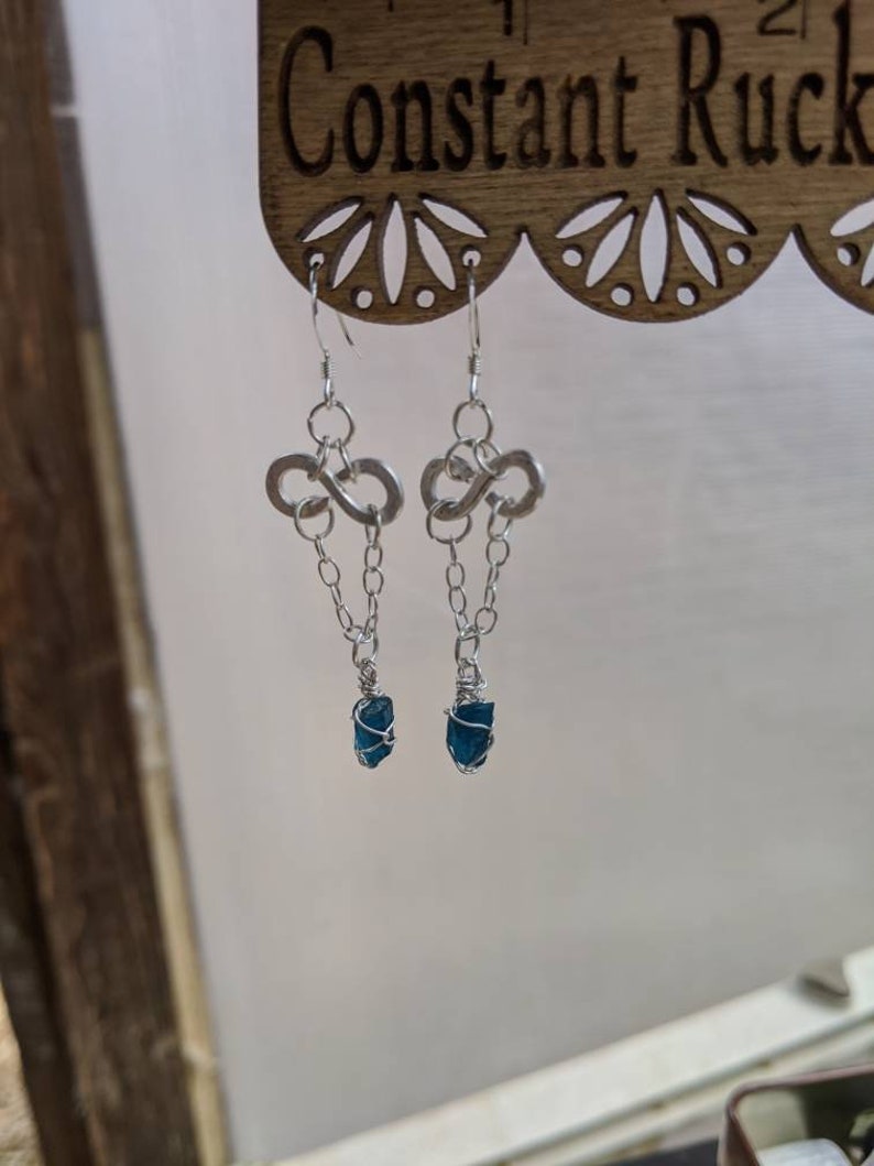 May include: A pair of silver infinity symbol earrings with a dangling chain and a dark blue gemstone at the end of each chain.