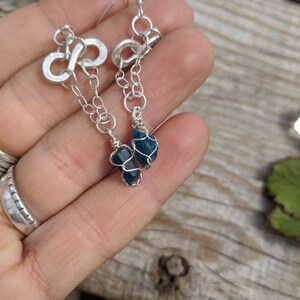 May include: Silver infinity symbol earrings with a dangling chain and a teal blue gemstone at the end.