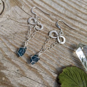 May include: A pair of silver earrings with infinity symbol charms and dangling blue crystal stones.