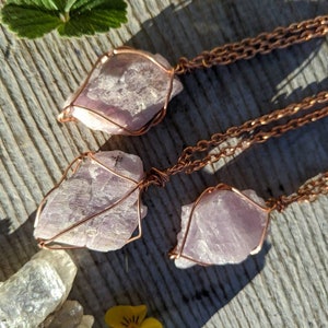 May include: Three pink crystal pendants wrapped in copper wire, hanging from copper chains. The crystals are raw and have a natural, irregular shape.