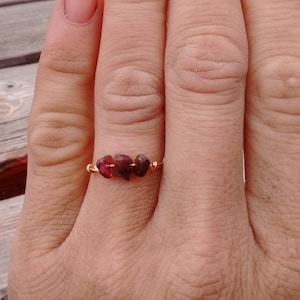 May include: A gold ring with three small, dark red gemstones set in a row.