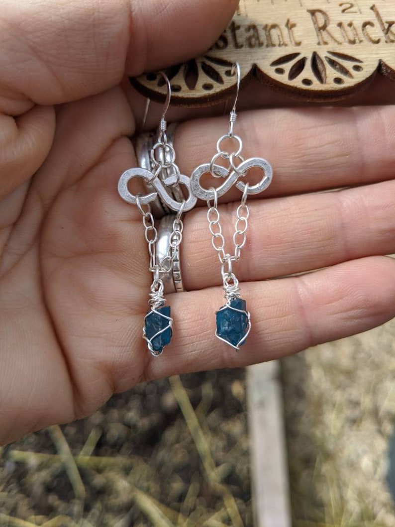 May include: Silver infinity earrings with a dangling blue gemstone wrapped in silver wire.