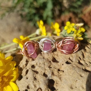 May include: Three wire-wrapped rings with pink gemstones. The rings are made with copper and silver wire. The gemstones are set in a wire cage.