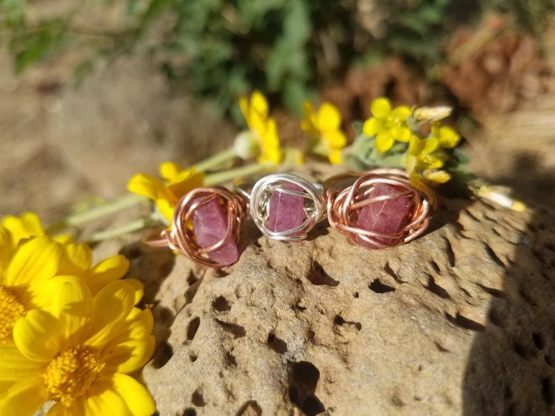 May include: Three wire-wrapped rings with pink gemstones. The rings are made with copper and silver wire. The gemstones are set in a wire cage.