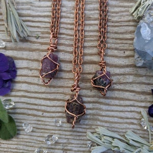 May include: Three copper wire wrapped pendants with raw purple gemstones. The pendants are hanging from copper chains.