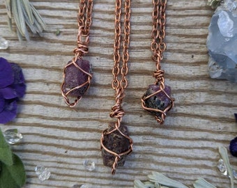 May include: Three copper wire wrapped pendants with raw purple gemstones. The pendants are hanging from copper chains.
