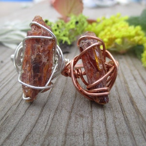 May include: Two rings with a brown crystal wrapped in wire. One ring is wrapped in silver wire and the other is wrapped in copper wire.