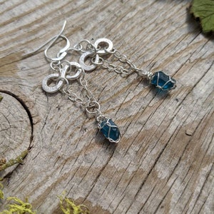 May include: Silver infinity symbol earrings with a dangling blue gemstone wrapped in silver wire.