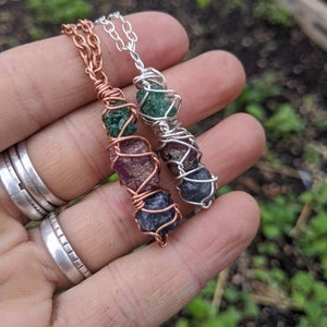 May include: Two wire-wrapped necklaces with different colored gemstones. The necklace on the left has a copper wire and features green, pink, and blue gemstones. The necklace on the right has a silver wire and features green and blue gemstones.