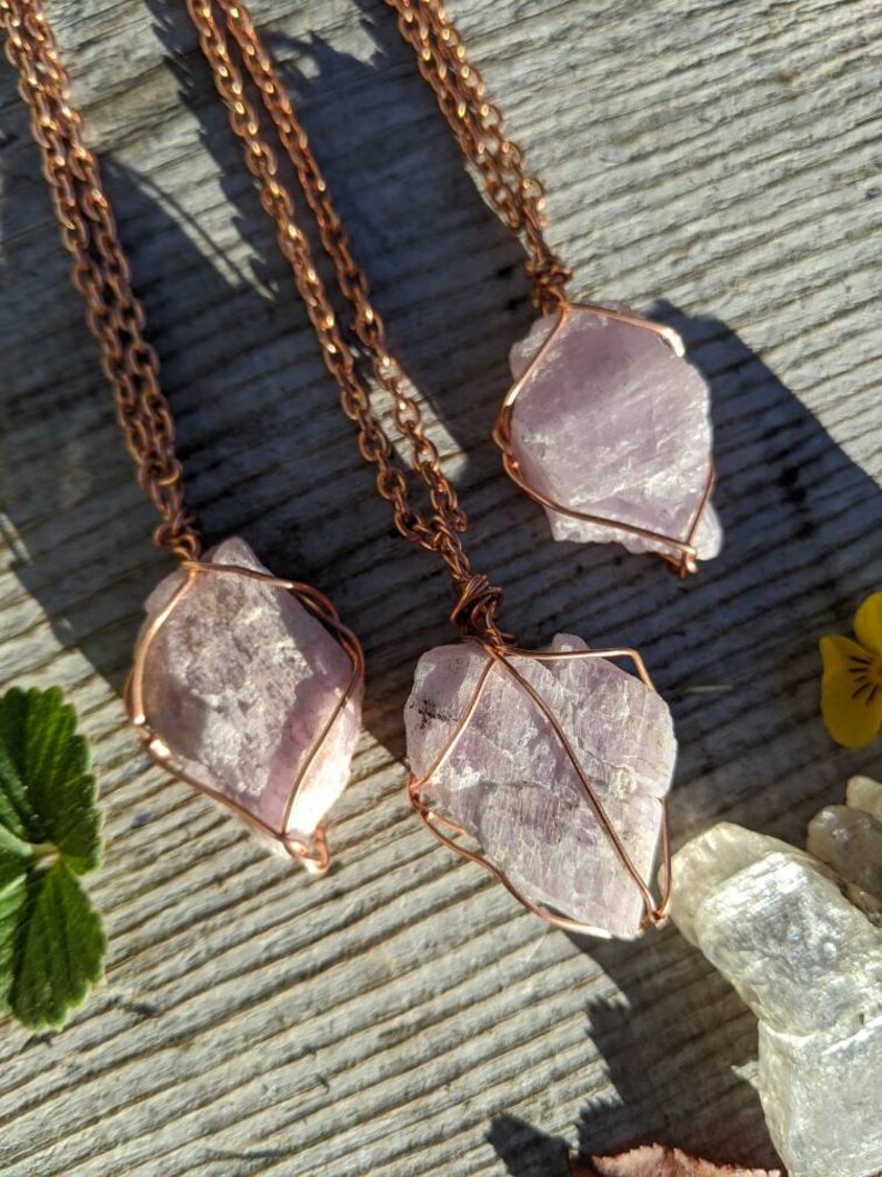 May include: Three copper wire wrapped pendants featuring raw amethyst crystals. The amethyst crystals are a light purple color and have a natural, rough texture. The copper wire is a warm, reddish-brown color.