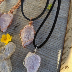May include: Two necklaces with pink crystal pendants wrapped in wire. The necklaces are on a wooden surface with a ruler in the background. One necklace has a copper wire wrap and the other has a silver wire wrap.