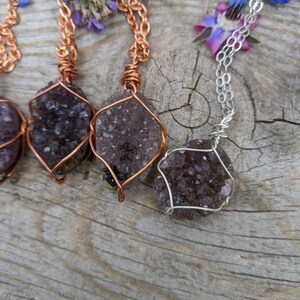 May include: Three amethyst crystal necklaces with copper and silver wire wrapping. The crystals are a deep purple color and have a rough, natural texture. The necklaces are displayed on a wooden surface.