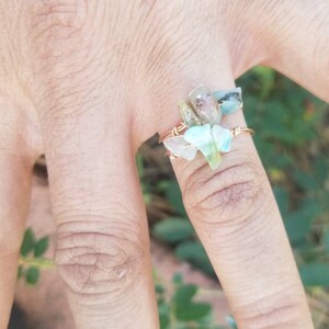 May include: A ring made with wire and small, clear, green, and brown stones. The ring is on a finger.