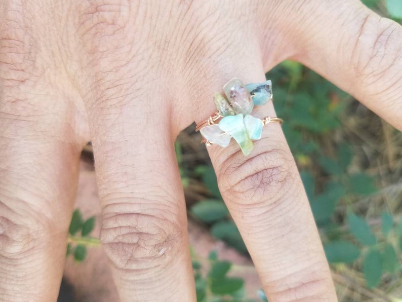 May include: A ring made with wire and small, clear, green, and brown stones. The ring is on a finger.