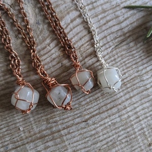 May include: Three necklaces with white gemstone pendants encased in wire cages. The necklaces are made with copper and silver chains.