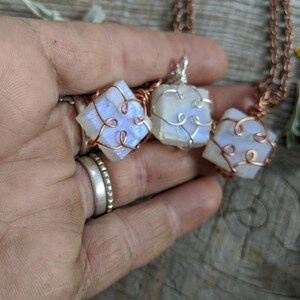 Puede incluir: Tres colgantes de piedra lunar iridiscente envueltos en alambre de cobre, cada uno con un dise&ntilde;o &uacute;nico. Los colgantes cuelgan de una cadena de cobre.