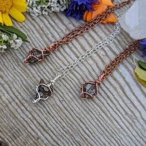 Puede incluir: Tres collares con cadenas de diferentes colores y colgantes de cristal envueltos en alambre. Las cadenas son de cobre, plata y cobre. Los cristales son de color gris oscuro y tienen una textura rugosa y natural.