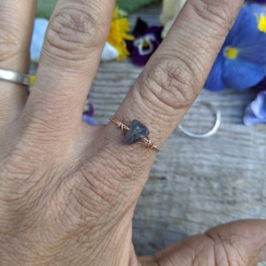 May include: A simple ring with a small, dark gray stone set in a copper wire band.