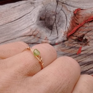 May include: A gold wire ring with a small green gemstone. The ring is on a finger.
