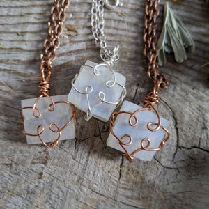 Puede incluir: Tres collares con colgantes de piedra blanca envueltos en alambre. Los collares est&aacute;n sobre una superficie de madera. El alambre es de cobre y plata.