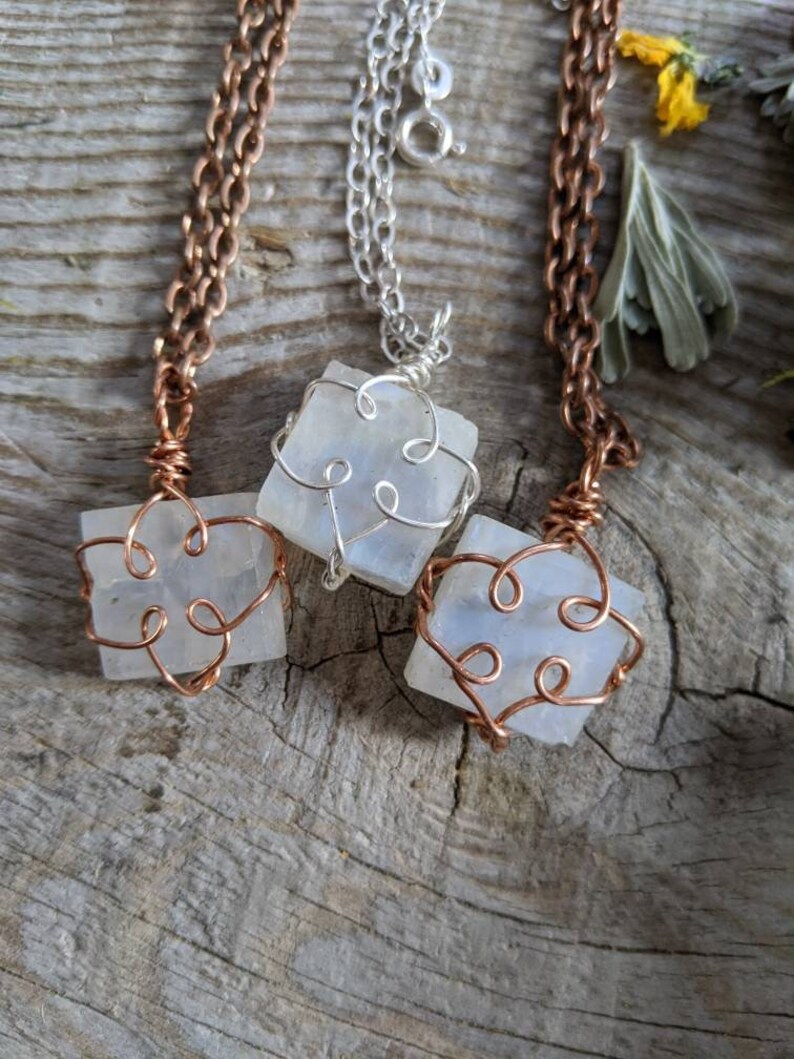 Puede incluir: Tres collares con colgantes de piedra blanca envueltos en alambre. Los collares est&aacute;n sobre una superficie de madera. El alambre es de cobre y plata.