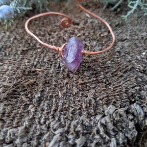 May include: A copper wire bracelet with a purple amethyst stone wrapped in the wire.