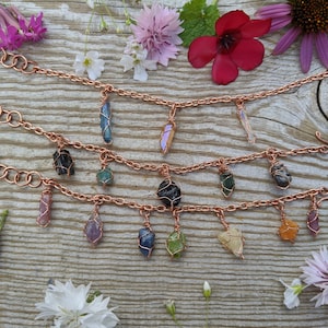 Pode incluir: Três pulseiras de corrente de cobre com pingentes de pedras preciosas de várias cores. Os pingentes são envoltos em fio de cobre e incluem ametista, quartzo rosa, aventurina verde, apatita azul, turmalina negra e quartzo transparente.