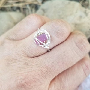 May include: A silver wire ring with a pink crystal encased in the center.