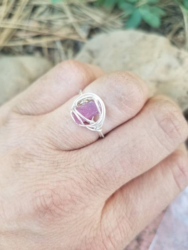 May include: A silver wire ring with a pink crystal encased in the center.