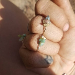 May include: Two rings with small green and blue stones wrapped in wire. The rings are on a person's finger.