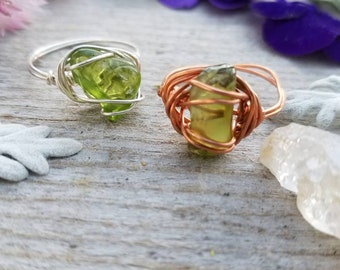 May include: Two wire-wrapped rings with green gemstone accents. The ring on the left is silver and the ring on the right is copper.