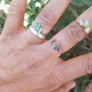 May include: Two rings with wire wrapped around them and small green and blue stones. The rings are on a person's hand.