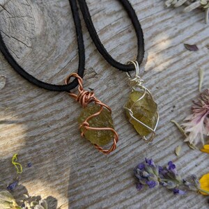 May include: Two necklaces with green crystal pendants wrapped in wire. One necklace has a copper wire wrap and the other has a silver wire wrap. Both necklaces have black suede cords.