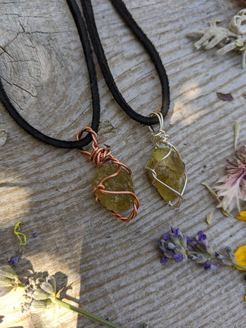 May include: Two necklaces with green crystal pendants wrapped in wire. One necklace has a copper wire wrap and the other has a silver wire wrap. Both necklaces have black suede cords.