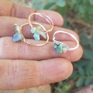 May include: Three gold rings with green and blue gemstone accents. The rings are made with wire and feature different sized gemstones.