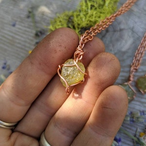 May include: A copper wire wrapped pendant featuring a yellow-green crystal. The pendant is hanging from a copper chain.