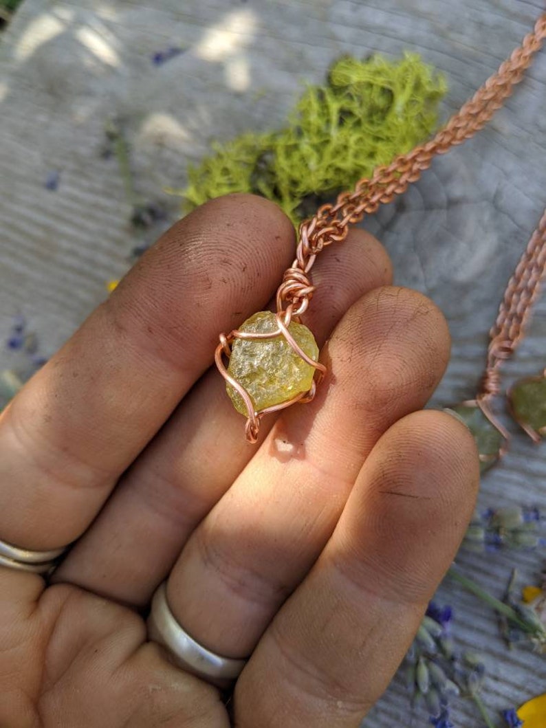 May include: A copper wire wrapped pendant featuring a yellow-green crystal. The pendant is hanging from a copper chain.