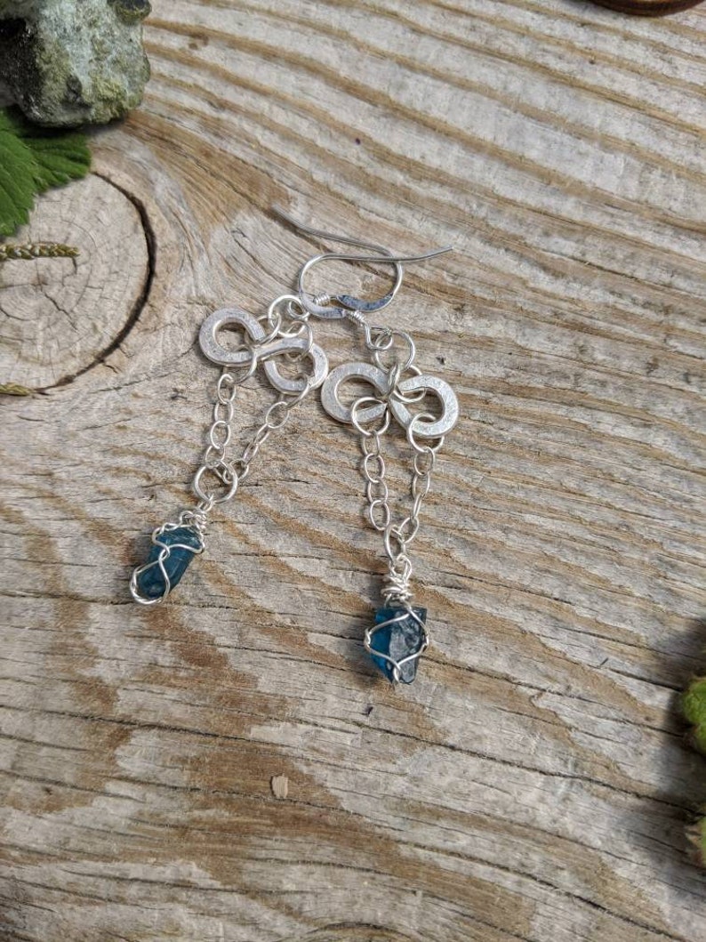 May include: A pair of silver earrings with infinity symbol charms and blue crystal accents.