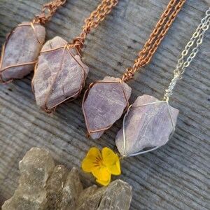 May include: Three necklaces with pink crystal pendants wrapped in copper wire. The necklaces are on a wooden surface with a yellow flower.